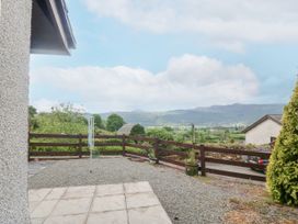 An outdoor patio area with gravel ground and a wooden fence overlooking a valley with hills and houses at Y Stabal in Llanddoged near Llanrwst