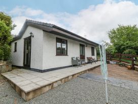 A single story house with a tiled patio and outdoor chairs near a gravel driveway and wooden fence at Y Stabal in Llanddoged near Llanrwst