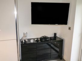 A wall-mounted television above a black cabinet with gaming console and decorative items at Sunnydene in Paignton