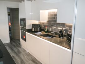 A kitchen with white cabinets black countertop black appliances and a gray tiled backsplash at Sunnydene in Paignton