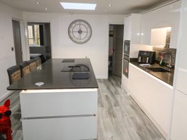 A modern kitchen with a black countertop island and stools a large wall clock and white cabinetry at Sunnydene in Paignton