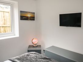 A bedroom corner with a window a glowing globe on a bedside table a wall mounted tv and a low cabinet at Sunnydene in Paignton