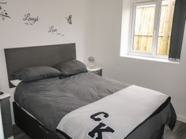 A bedroom with a double bed with dark gray bedding a window and wall decals with words at Sunnydene in Paignton