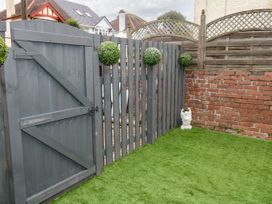 A fenced outdoor area with artificial grass a gray wooden gate three round green shrubs on the fence a small white statue near a brick wall at Sunnydene in Paignton