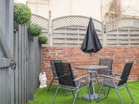 A small outdoor seating area with four chairs around a table with a closed umbrella on artificial grass at Sunnydene in Paignton