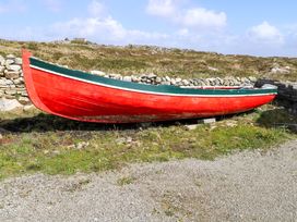 A red boat on land surrounded by grass and stone wall at Tí Tom Nárta, Trabane near Lettermore, County Galway