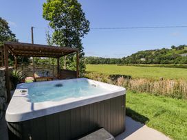 A hot tub situated next to a wooden pergola in a field at Plas Glan Yr Afon in Llangernyw