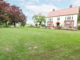 A large lawn with trees and a two-story house with a tiled roof at High House in Southrepps
