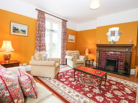 A living room with beige armchairs a wooden coffee table red patterned rug and a fireplace at High House in Southrepps