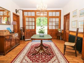 A room with wooden doors and floor a table with a plant in the center and a red patterned rug at High House in Southrepps