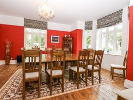 A dining room with a wooden table and chairs on a patterned rug with red walls and windows at High House in Southrepps