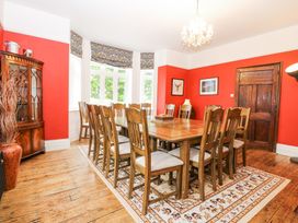 A dining room with a wooden table and twelve chairs on a patterned rug and red walls at High House in Southrepps