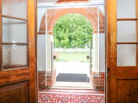 An entrance with wooden doors opening to a glass door and a brick archway overlooking a lawn and trees at High House in Southrepps