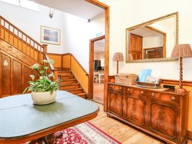A foyer with a wooden staircase a table with a potted plant a sideboard with lamps and a mirror at High House in Southrepps