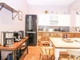 A kitchen with wooden chairs a wooden table a black refrigerator a wooden sideboard appliances and white cabinets at High House in Southrepps