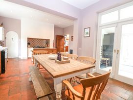 A kitchen dining area with a wooden table, chairs, bench, tiled floor, and glass doors at High House in Southrepps