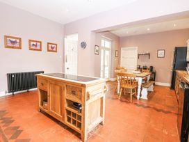 A kitchen with a wooden island in the center a dining table with chairs and bench and framed pictures on the walls at High House in Southrepps