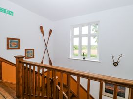 A staircase with wooden railing and walls decorated with crossed oars paintings and a mounted antler at High House in Southrepps