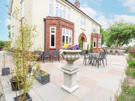 An outdoor patio with tables chairs potted plants and a large flower urn at High House Southrepps