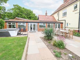 An outdoor patio area with a hot tub wooden dining table and chairs plants and a tiled walkway at High House in Southrepps