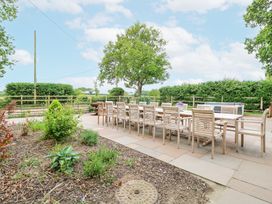 An outdoor patio with a long wooden dining table and chairs surrounded by plants and trees at High House in Southrepps