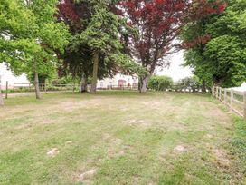A grassy yard with trees and a fence with a house in the background at High House in Southrepps