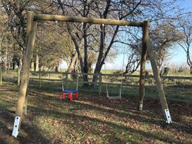 A swing set with one blue swing and one red swing in an outdoor area at High House Southrepps