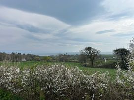 A rural landscape with flowering bushes in the foreground green fields trees houses and a body of water in the distance at Min Y Mor in Llanystumdwy near Criccieth