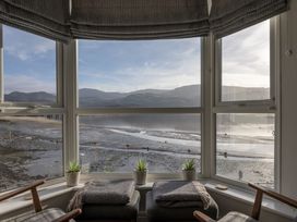A bay window with stools blankets small plants and chairs overlooking a tidal shore with hills in the distance at Harbour View - Flat 2 in Barmouth