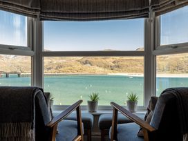 Two chairs with cushions facing a bay window with potted plants on the sill overlooking a body of water and hills at Harbour View - Flat 2 in Barmouth