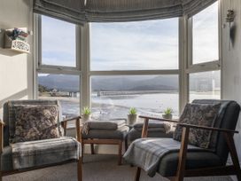 A sitting area with two chairs and two footstools by a large window overlooking water and mountains at Harbour View - Flat 2 in Barmouth