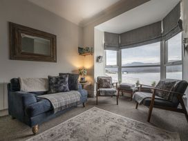 A sitting room with a sofa chairs by a large window overlooking water and a bridge at Harbour View - Flat 2 in Barmouth