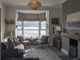 A living room with armchairs sofa television and a large window overlooking a body of water at Harbour View - Flat 2 in Barmouth