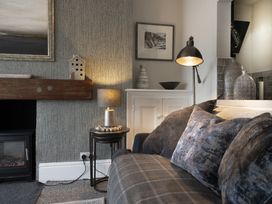 A living room corner with a plaid sofa, cushions, a lamp on nested tables, fireplace, and decorative vases at Harbour View - Flat 2 in Barmouth