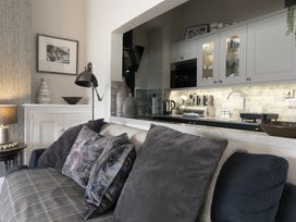 A living room with a sofa and cushions next to a kitchen with cabinets and countertop at Harbour View - Flat 2 in Barmouth