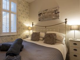 A bedroom with a double bed two bedside tables with lamps and a window with white shutters at Harbour View - Flat 2 in Barmouth