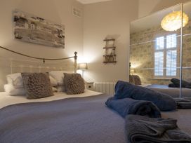 A bedroom with a bed with gray pillows and blue blankets a bedside table with a lamp a wall mirror and window shutters at Harbour View - Flat 2 in Barmouth