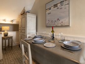 A dining table set with dishes glasses and cutlery beside a cupboard and lamp in Harbour View - Flat 2 in Barmouth