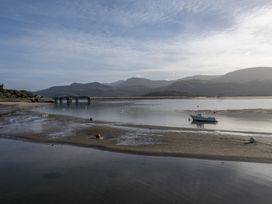 A river with a small boat and a bridge with mountains in the background at Harbour View - Flat 2 in Barmouth