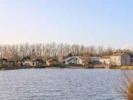 The view of cabins and a stone building by a lake at Curlew Lodge in Carnforth