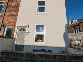 Front exterior of a white brick house with two windows and a green door behind a low brick wall at Pipit House in Whitby