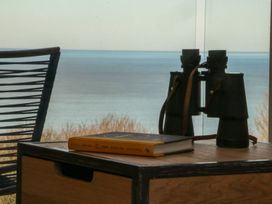 A table with binoculars and a book beside a chair and a view of the sea at The Lookout