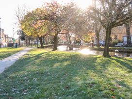 A park with a path, grass, trees, and a bridge near a canal at Mallards in Bourton-On-The-Water