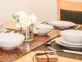 A dining table set with white bowls and plates cutlery and a small flower arrangement at Gerrard House Apartment in Llandudno