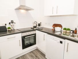 A kitchen with white cabinets a stove oven dishwasher kettle and plants at Gerrard House Apartment in Llandudno