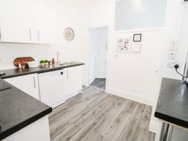 A kitchen with white cabinets black countertops a clock sink and wall art at Gerrard House Apartment in Llandudno