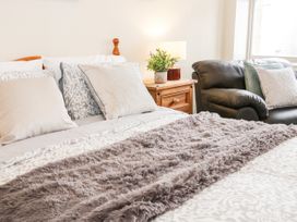 A bed with pillows and a furry throw blanket next to a wooden nightstand with a lamp and plant and a leather sofa with cushions at Gerrard House Apartment in Llandudno