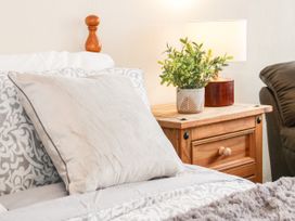 A bedroom with a bed pillow a wooden nightstand a table lamp and a potted plant at Gerrard House Apartment in Llandudno