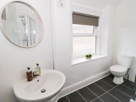 A bathroom with a sink mirror toilet window with blinds and two small plants on the sill at Gerrard House Apartment in Llandudno