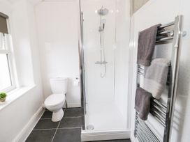 A bathroom with a shower enclosure toilet window and towel rack with towels at Gerrard House Apartment in Llandudno